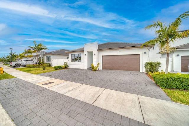 view of front of home with stucco siding, decorative driveway, fence, and a garage