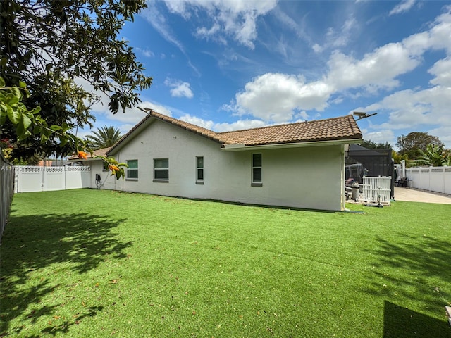back of house with a fenced backyard, stucco siding, a yard, and a tiled roof
