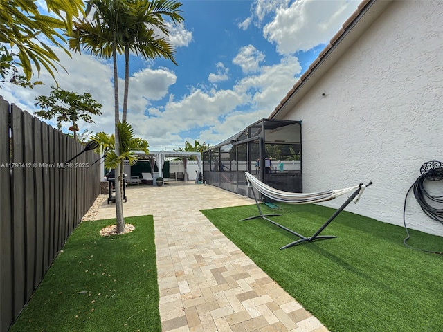 view of yard featuring glass enclosure, a fenced backyard, and a patio area