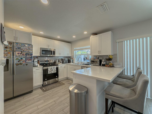 kitchen featuring decorative backsplash, stainless steel appliances, a sink, visible vents, and a peninsula