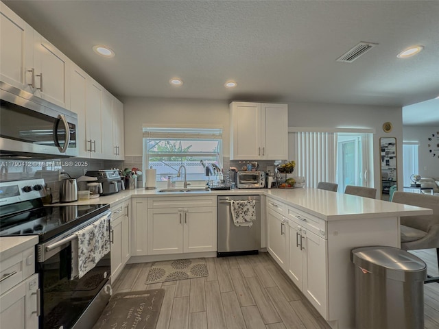kitchen featuring decorative backsplash, a sink, appliances with stainless steel finishes, recessed lighting, and a peninsula
