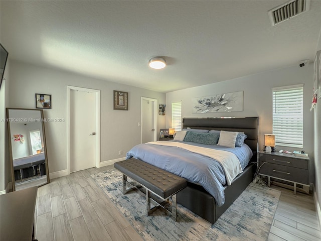 bedroom with baseboards, visible vents, wood finish floors, and a textured ceiling