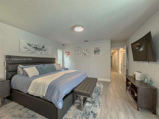 bedroom featuring a textured ceiling, visible vents, light wood-type flooring, and baseboards