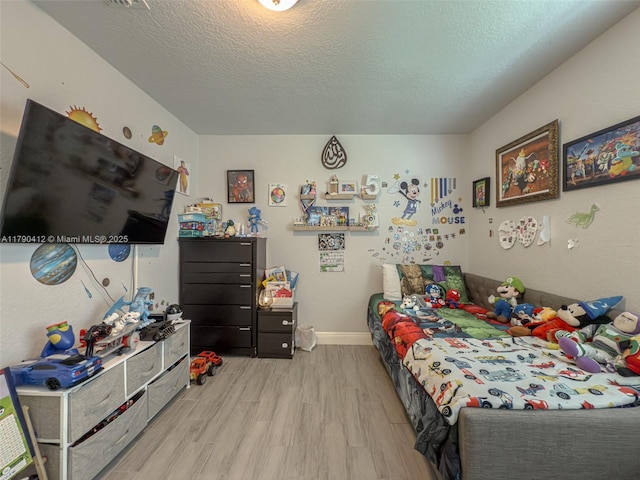 bedroom featuring baseboards, wood finished floors, and a textured ceiling