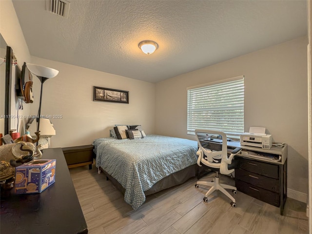 bedroom with a textured ceiling, wood finished floors, and visible vents