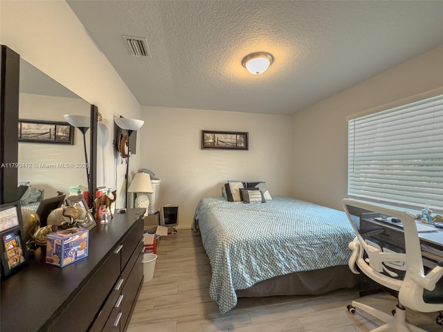 bedroom featuring light wood-style floors, visible vents, a textured ceiling, and baseboards