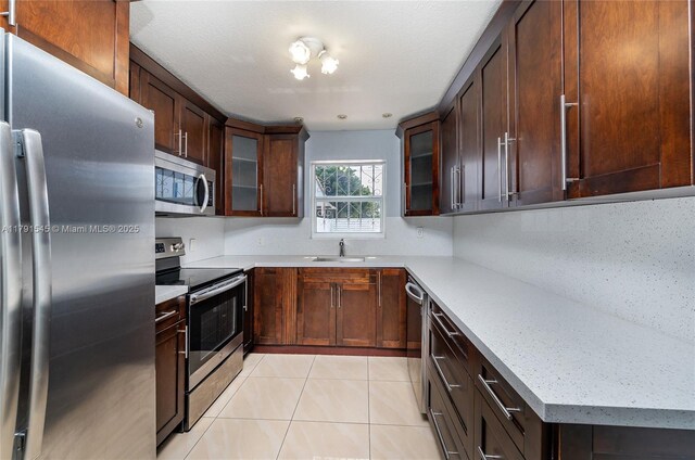 kitchen with a sink, appliances with stainless steel finishes, glass insert cabinets, and light tile patterned floors