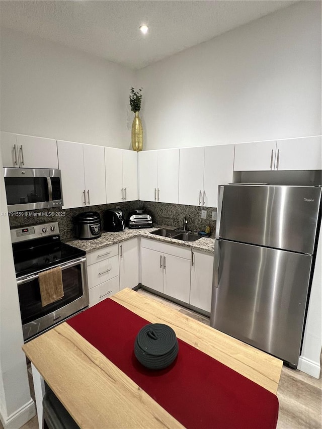 kitchen featuring tasteful backsplash, white cabinetry, stainless steel appliances, and a sink