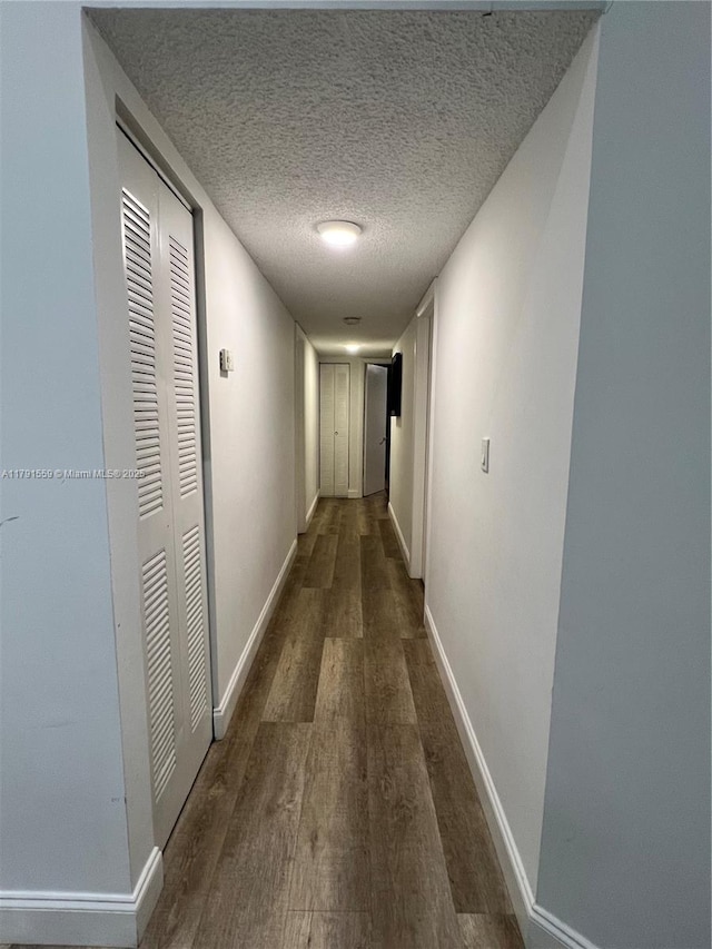 corridor with a textured ceiling, wood finished floors, and baseboards