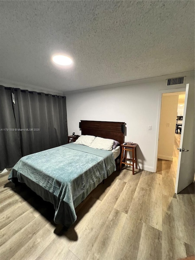 bedroom featuring baseboards, visible vents, wood finished floors, and a textured ceiling