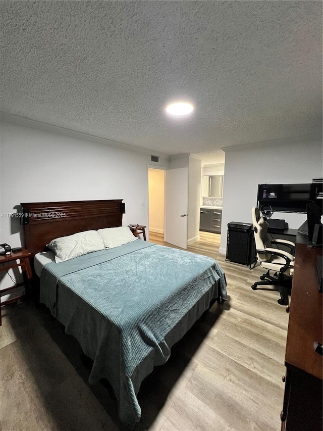 bedroom with a textured ceiling, visible vents, ensuite bathroom, and light wood-style flooring
