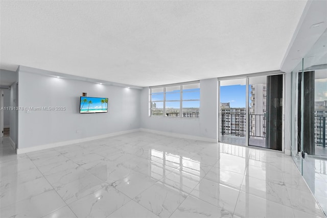 empty room with a textured ceiling, marble finish floor, and baseboards