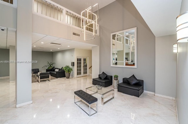 living area featuring baseboards, visible vents, a notable chandelier, and a high ceiling
