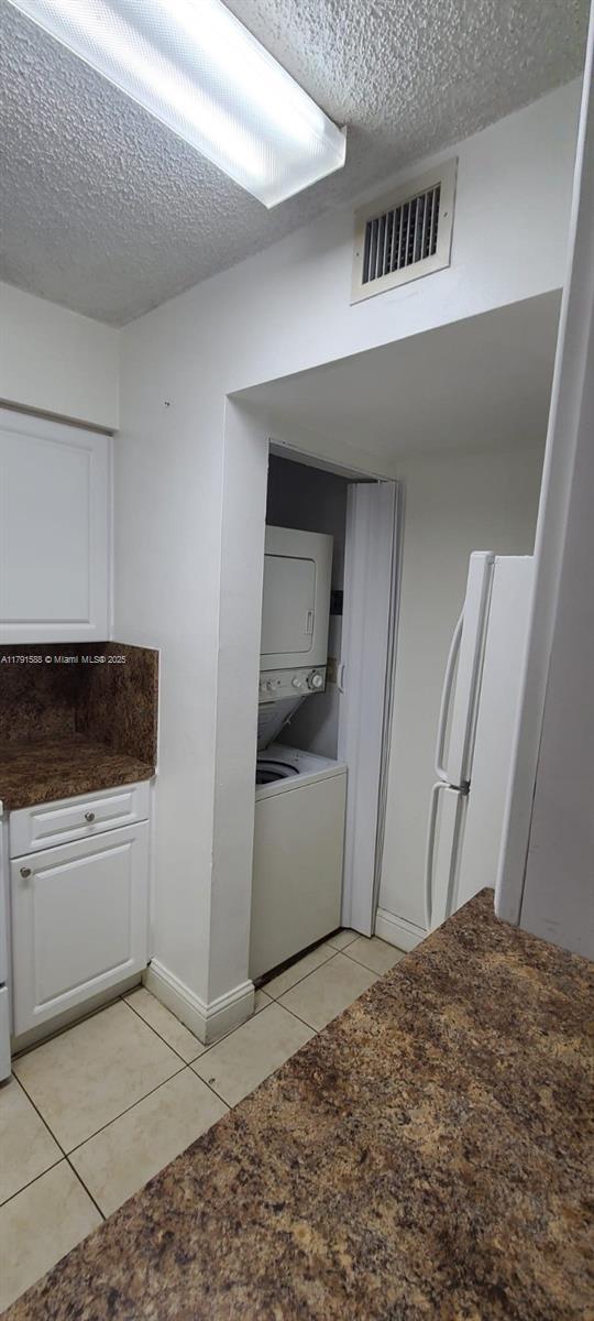 15231 SW 80th St Unit 209, Miami, FL 33193 - kitchen with stacked washer and dryer, light tile patterned floors, white cabinetry, visible vents, and freestanding refrigerator