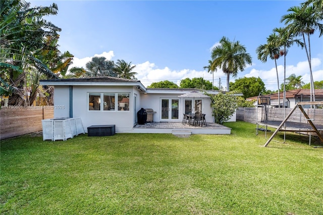 back of house with a trampoline, french doors, a fenced backyard, and stucco siding