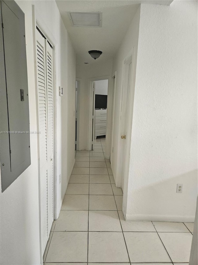 hallway featuring light tile patterned flooring, attic access, and electric panel
