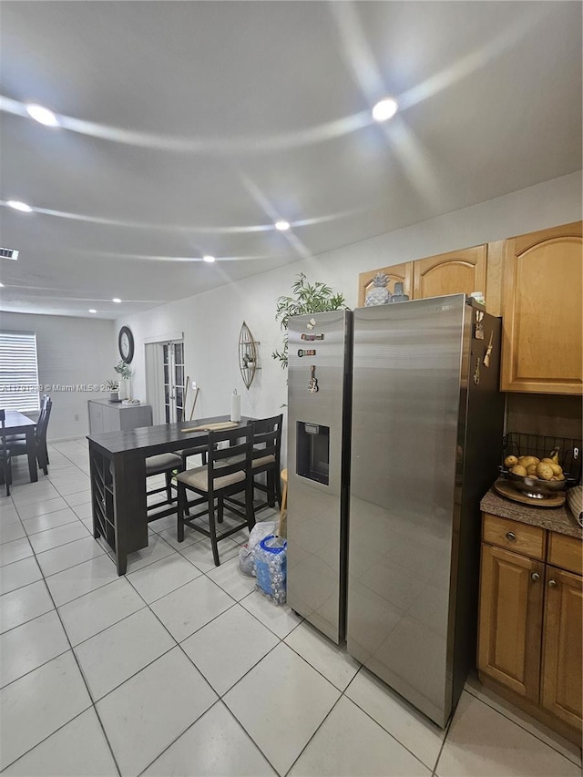 kitchen featuring light tile patterned floors, dark countertops, visible vents, and stainless steel refrigerator with ice dispenser
