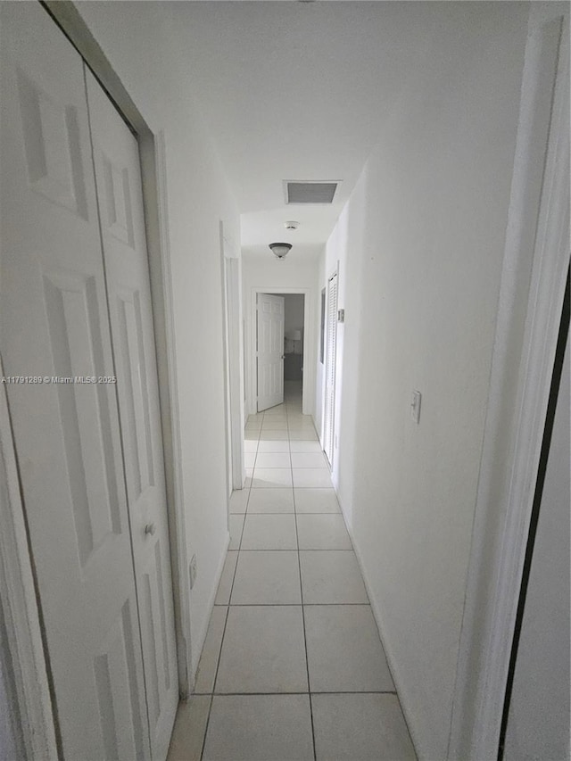 hall featuring baseboards, visible vents, and light tile patterned flooring