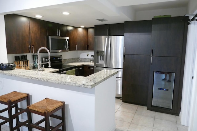 kitchen with light stone countertops, light tile patterned flooring, visible vents, a peninsula, and appliances with stainless steel finishes