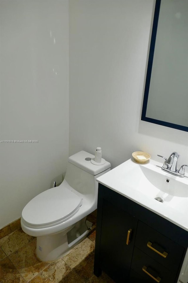 bathroom with toilet, stone tile flooring, and vanity