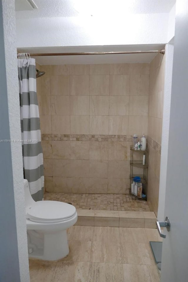 bathroom with tile patterned floors, tiled shower, and toilet