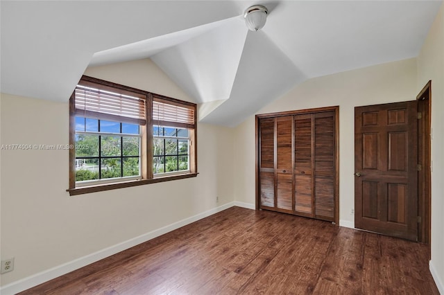 unfurnished bedroom featuring a closet, dark wood-style flooring, baseboards, and vaulted ceiling