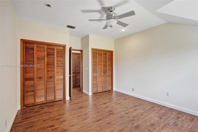 unfurnished bedroom featuring baseboards, two closets, wood finished floors, and visible vents