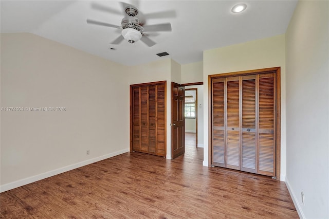unfurnished bedroom with two closets, baseboards, visible vents, and light wood-style floors