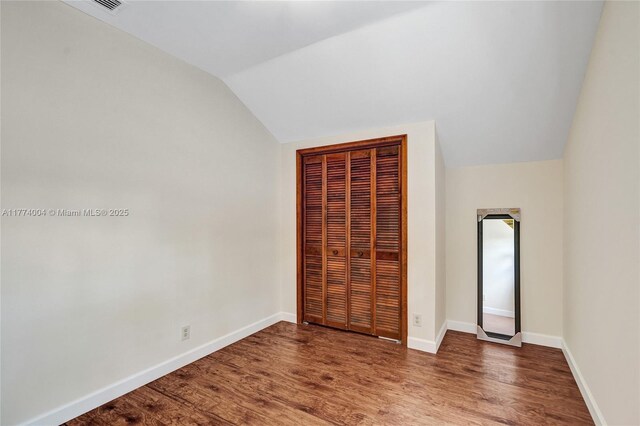 unfurnished bedroom with a closet, baseboards, vaulted ceiling, and wood finished floors