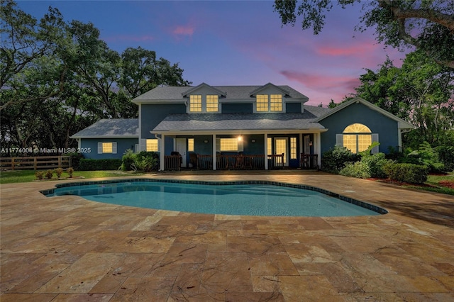 rear view of property with a porch, an outdoor pool, fence, and stucco siding