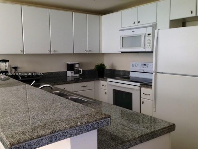 kitchen with a peninsula, a sink, white cabinetry, and white appliances
