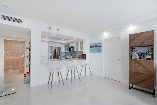 kitchen with white cabinets, glass insert cabinets, appliances with stainless steel finishes, a breakfast bar, and visible vents