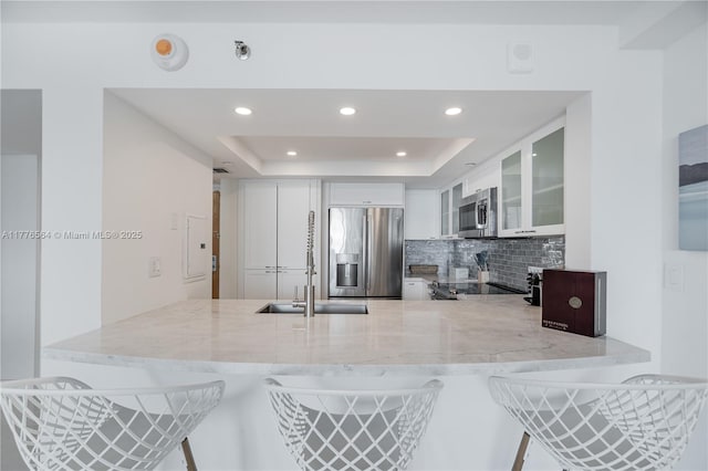 kitchen with light stone countertops, appliances with stainless steel finishes, backsplash, a sink, and a peninsula