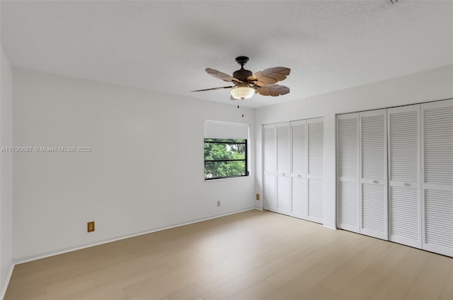 unfurnished bedroom featuring two closets, a ceiling fan, light wood-style flooring, and baseboards