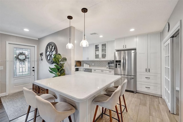 kitchen with a breakfast bar, visible vents, light wood-type flooring, and stainless steel fridge
