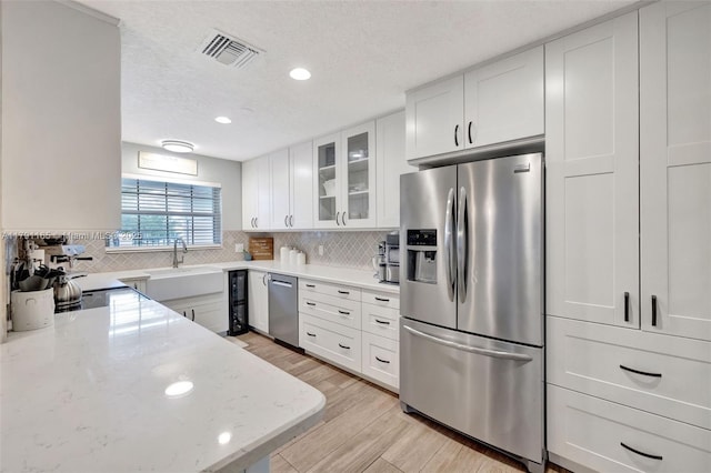 kitchen featuring glass insert cabinets, stainless steel appliances, backsplash, a sink, and white cabinetry