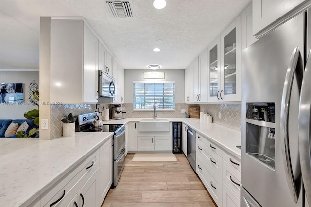 kitchen featuring a sink, light wood-style floors, glass insert cabinets, visible vents, and appliances with stainless steel finishes
