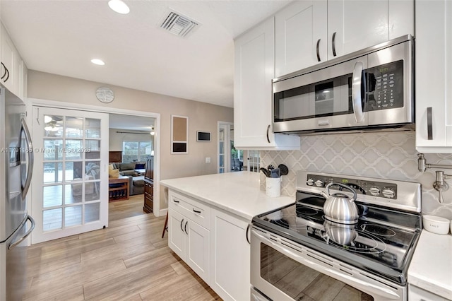 kitchen featuring stainless steel appliances, decorative backsplash, visible vents, white cabinetry, and light countertops