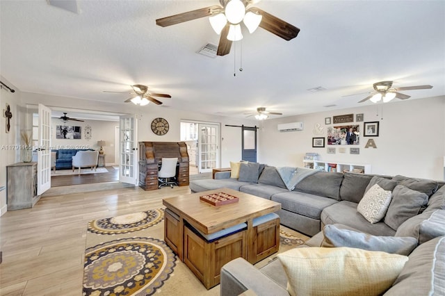 living room with light wood-type flooring, a wall mounted AC, visible vents, a ceiling fan, and french doors