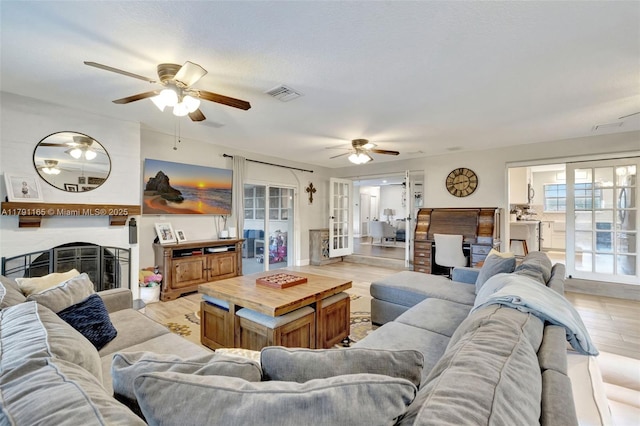 living area featuring a large fireplace, visible vents, ceiling fan, and light wood-style flooring