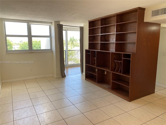 spare room with light tile patterned floors, visible vents, a textured ceiling, and baseboards
