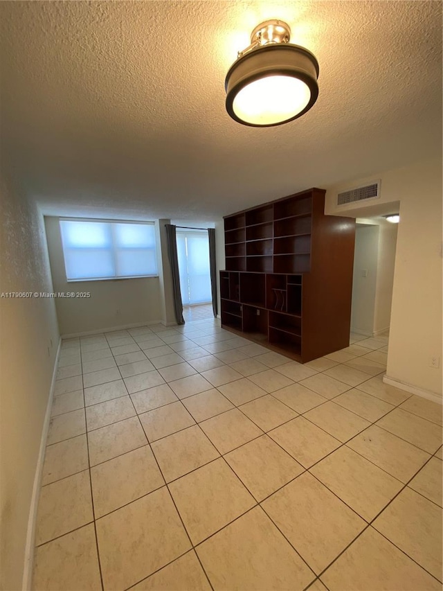 empty room with light tile patterned flooring, a textured ceiling, visible vents, and baseboards