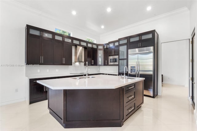 kitchen featuring crown molding, a sink, a spacious island, built in appliances, and wall chimney exhaust hood