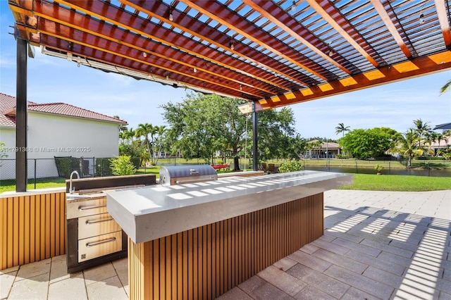 view of patio featuring exterior kitchen, grilling area, a pergola, a sink, and fence