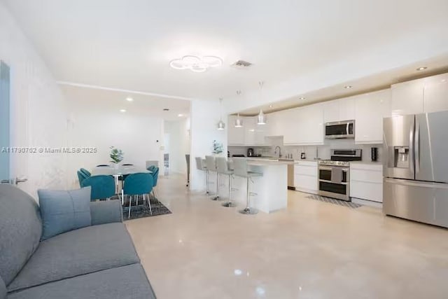 kitchen featuring white cabinets, appliances with stainless steel finishes, visible vents, a kitchen bar, and concrete flooring