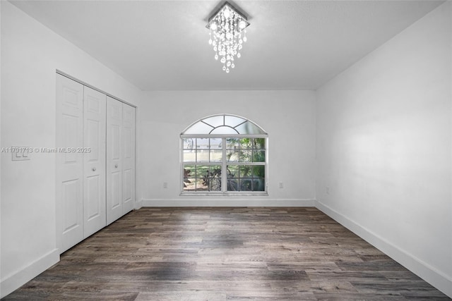 unfurnished bedroom with dark wood finished floors, baseboards, a notable chandelier, and a closet
