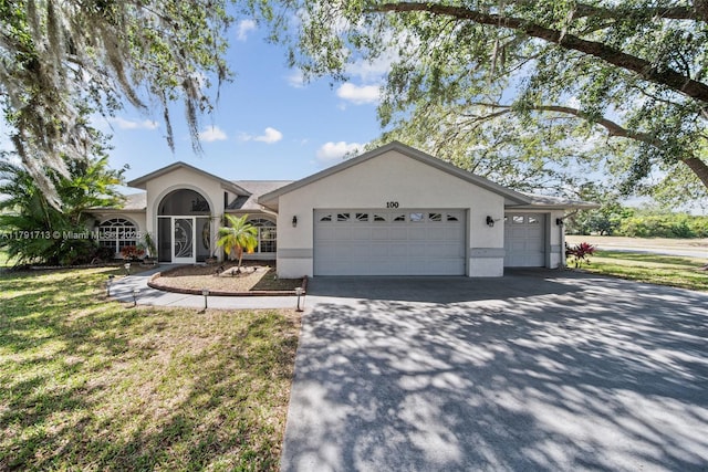 ranch-style home with a garage, a front lawn, stucco siding, and driveway
