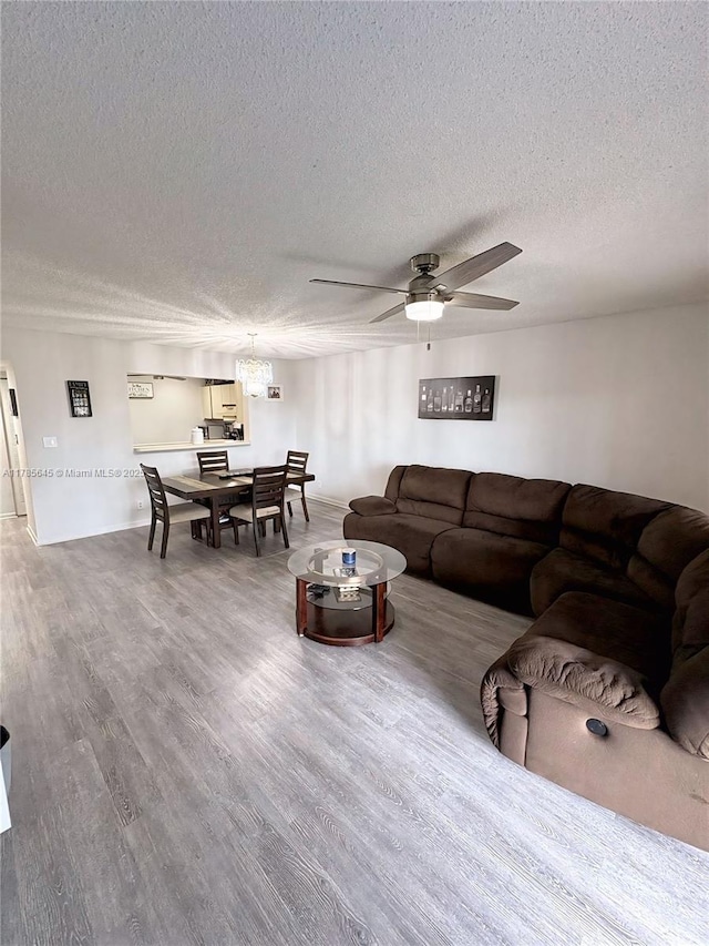 living room featuring baseboards, wood finished floors, ceiling fan, and a textured ceiling