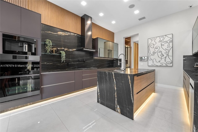 kitchen featuring dark stone countertops, a sink, visible vents, wall chimney exhaust hood, and modern cabinets