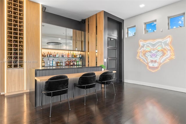bar with a bar, dark wood finished floors, and baseboards